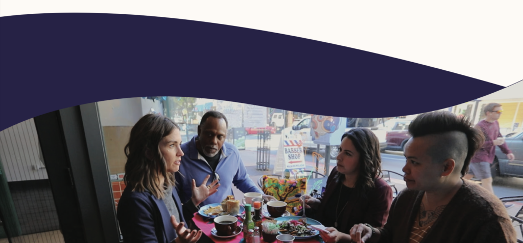 Four diverse Uplift team members eating a meal at a cafe together and talking animatedly